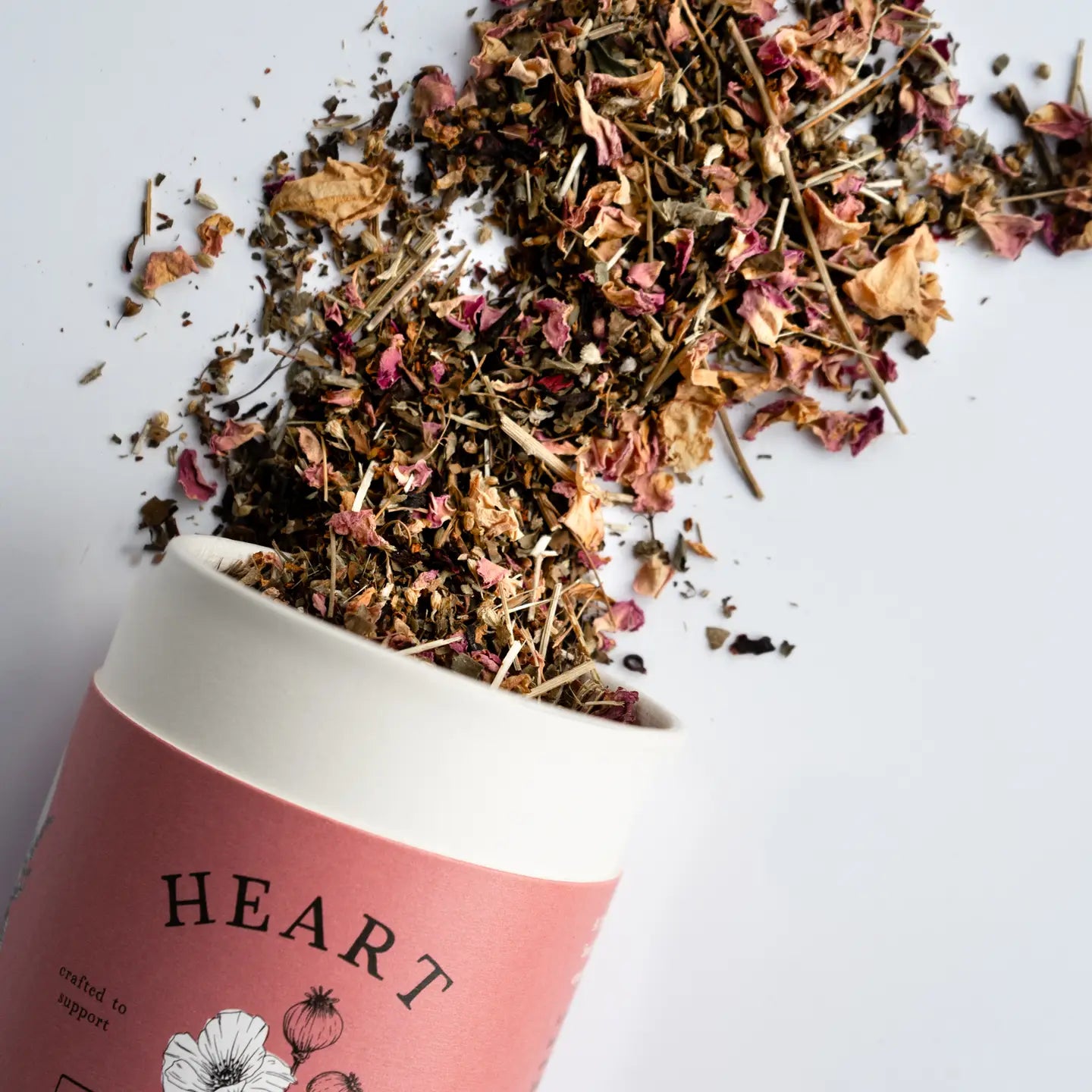 Tea leaves spilling out of a pink container labeled 'Heart' on a white background