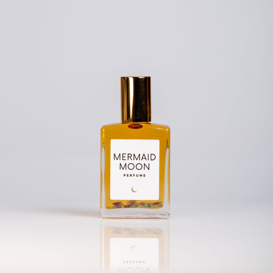A glass roller bottle of MERMAID MOON perfume with a gold cap, labeled with the product name and a crescent moon illustration.