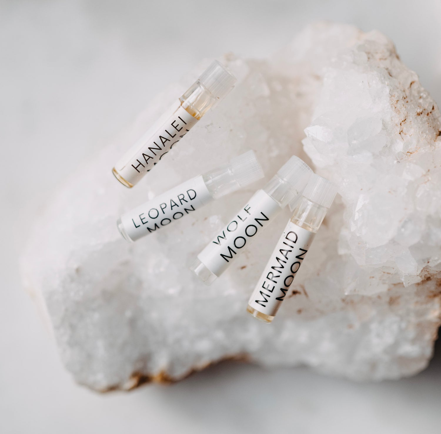 Four small glass bottles labeled 'Hanalei', 'Leopard Moon', 'Wolf Moon', and 'Mermaid Moon' on a textured white surface.