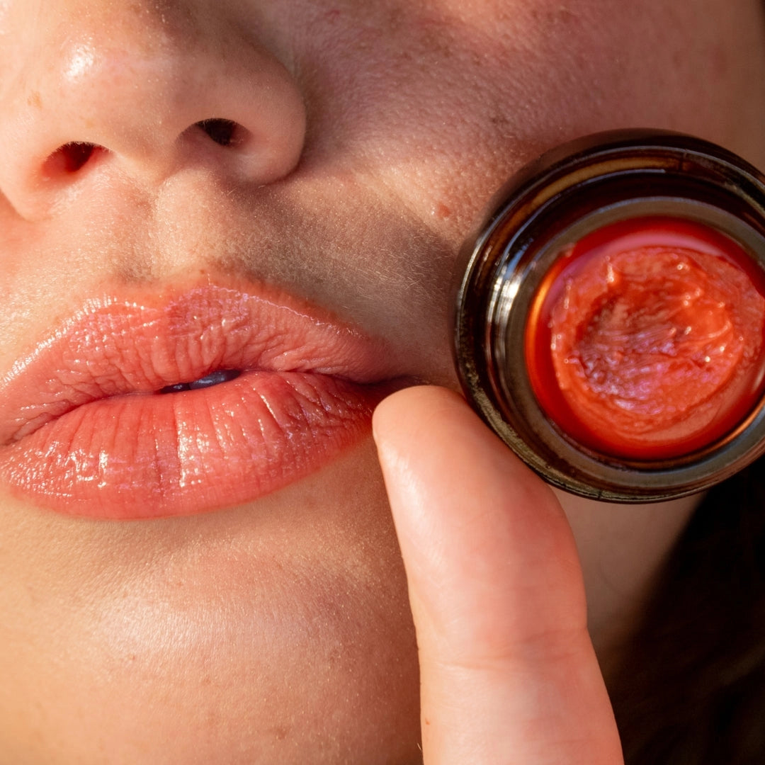 Close-up of a person applying red lip balm to their lips using a small mirror.